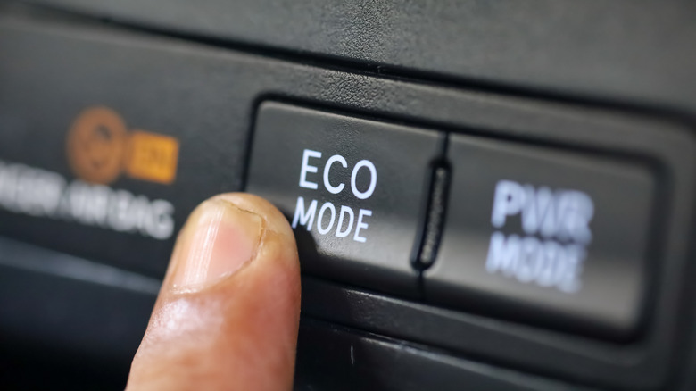 car driver pressing eco mode button on luxury car dashboard. eco mode is a relaxed and fuel efficient driving mode