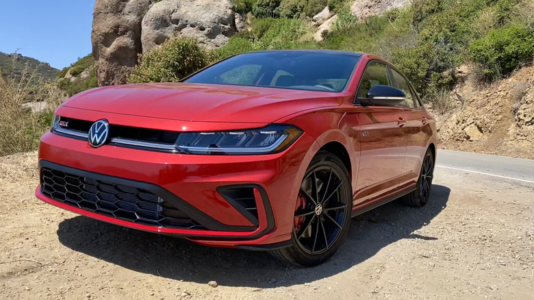 Front three quarters shot of a red Jetta GLI parked on dirt in front of a shrub covered mountainside