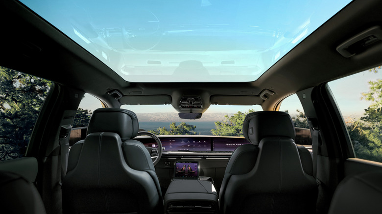 A front facing interior view of the Cadillac Escalade IQL with light coming in the panoramic moon roof, wide screen-laden dashboard and leather touchpoints.