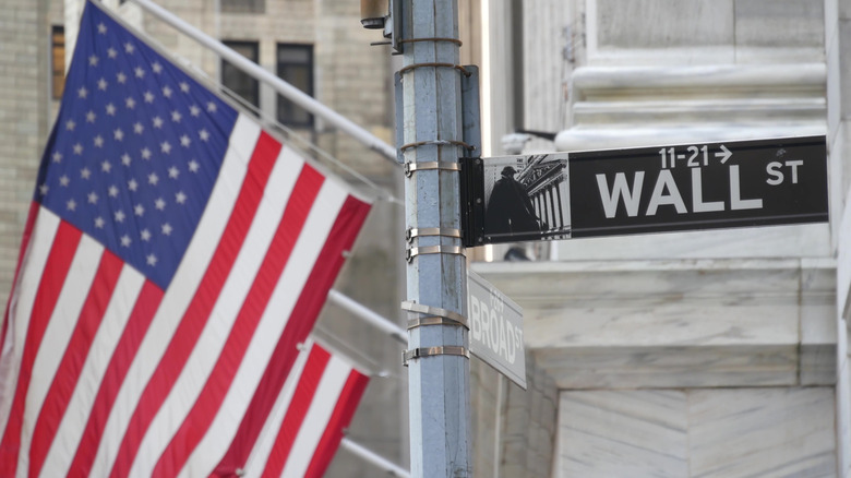 A cropped image of a street pole on New York City's Wall Street, with an American flag waving behidn it.