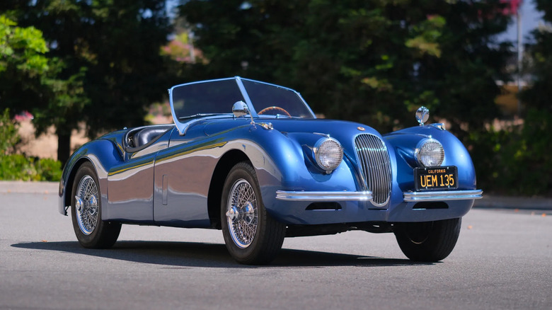 A front three-quarters shot of a blue '52 Jaguar XK120 Roadster parked in front of trees
