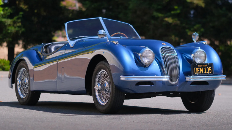 A front three-quarters shot of a blue '52 Jaguar XK120 Roadster parked in front of trees