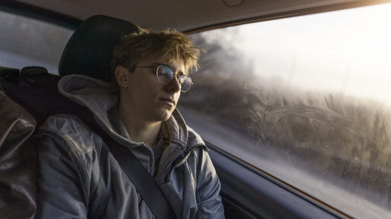 A teenage boy sleeping in the back seat of a car.