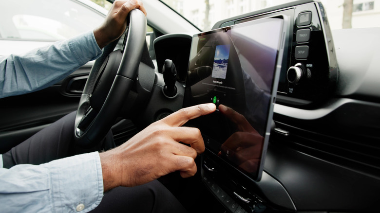 A man's finger reaches out to the car infotainment screen to make an adjustment