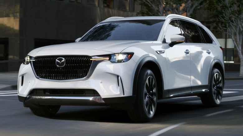 Mazda CX-90 Plug-in Hybrid Electric Vehicle driving down city street with a building in the background