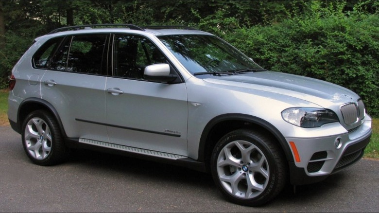 A silver 2011 BMW X5 parked with trees in the background