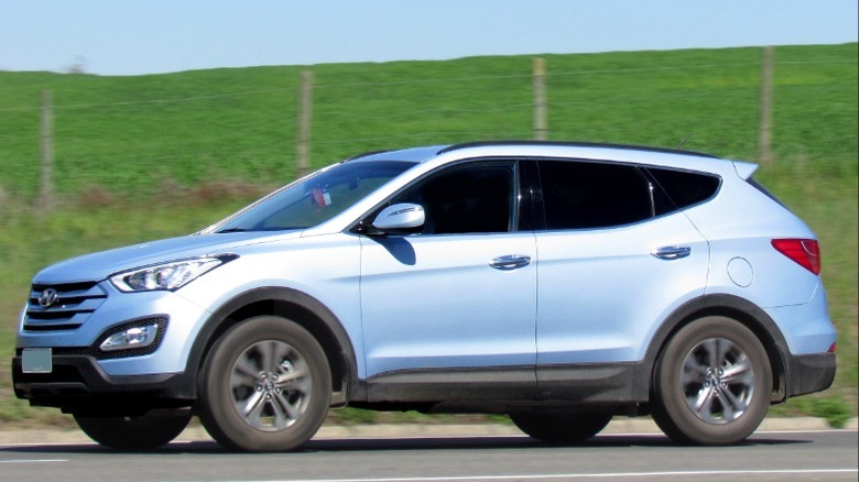 A light blue 2013 Hyundai Santa Fe driving in front of a grassy hill