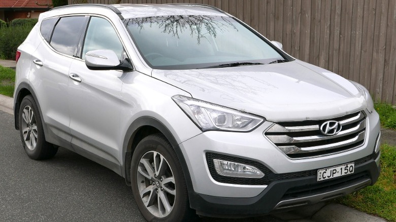A silver 2013 Hyundai Santa FE parked on a residential street in front of a wooden fence