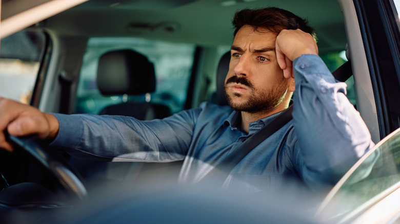 A man sits in his car, annoyed.