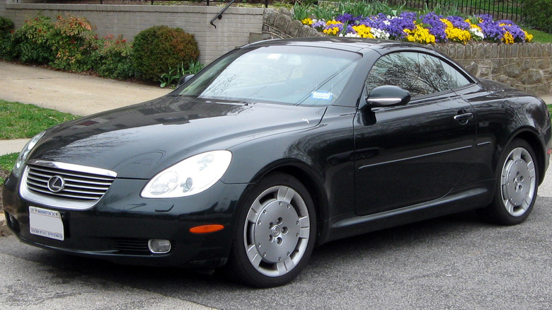 a black 2001 lexus sc parked on a neighborhood street with purple, yellow and white flowers in the background