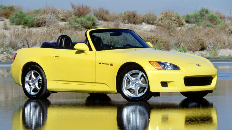 Front three-quarters shot of a bright yellow 2001 Honda S2000 parked on wet asphalt on a sunny day in front of desert shrubs