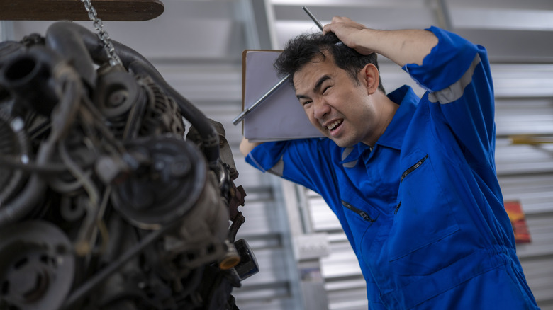 Asian mechanic in blue jumpsuit feeling frustrated with a difficult car engine problem  by: Wasana Kunpol
