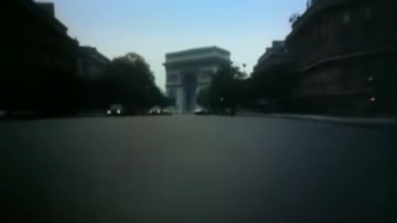 Shot from the front bumper of a car approaching the Arc de Triomphe