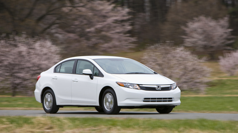 A white 2012 Honda Civic HF drives past a wooded area.