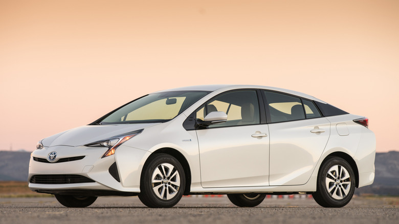 A white 2016 Toyota Prius Eco sits on an open stretch of flat pavement.