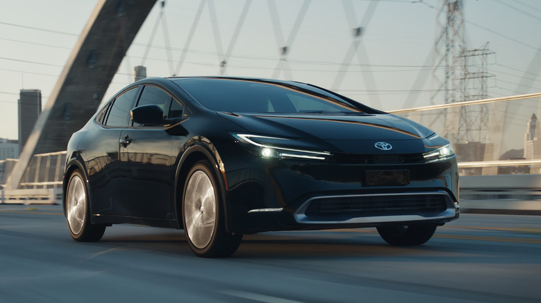 A black 2023 Toyota Prius drives across an urban bridge.