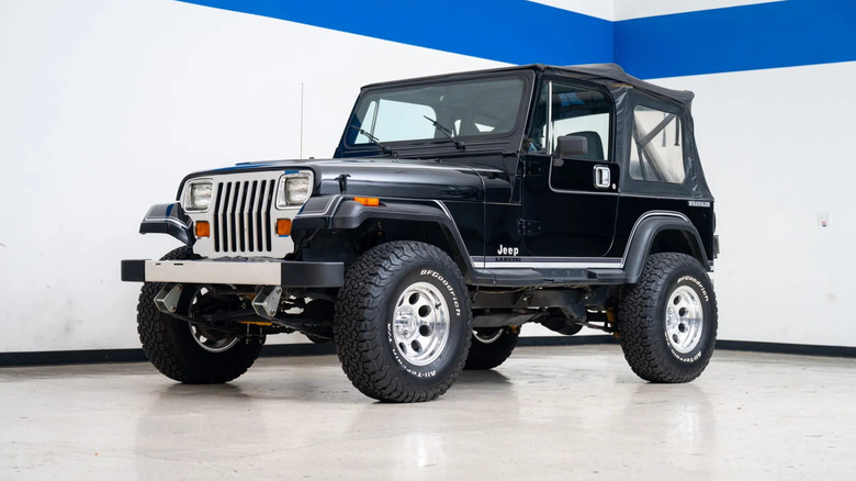 Front three quarters shot of a black Wrangler soft top in front of a white wall with a blue stripe on it