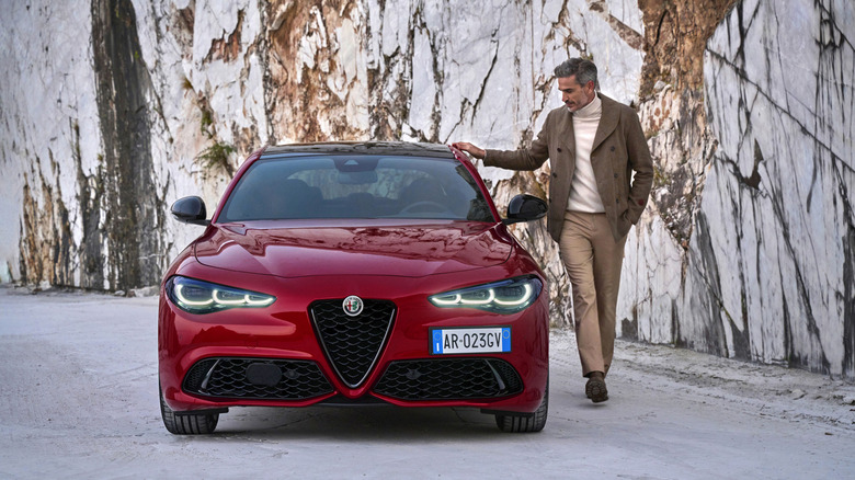 Front end of a red Alfa Romeo Giulia with a man touching it