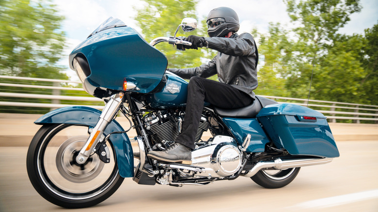 A close-up of someone dressed in all black riding a teal Harley Davidson Road Glide on a bridge past trees