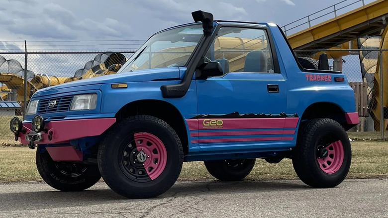 Front three quarters shot of a blurple and pink Geo Tracker parked in front of a yellow waterslide