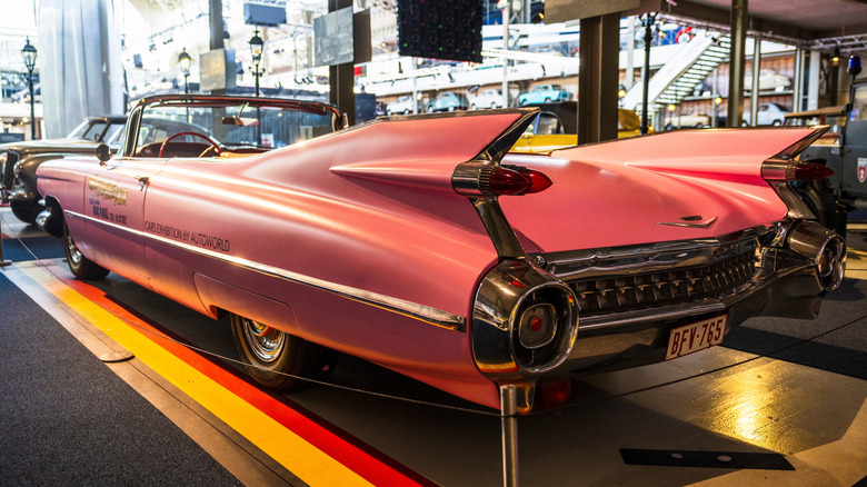 Brussels Belgium 2025-07-11 light pink 1959 Cadillac Series 62 Eldorado convertible with prominent chrome grille and large tail fins, displayed indoors.