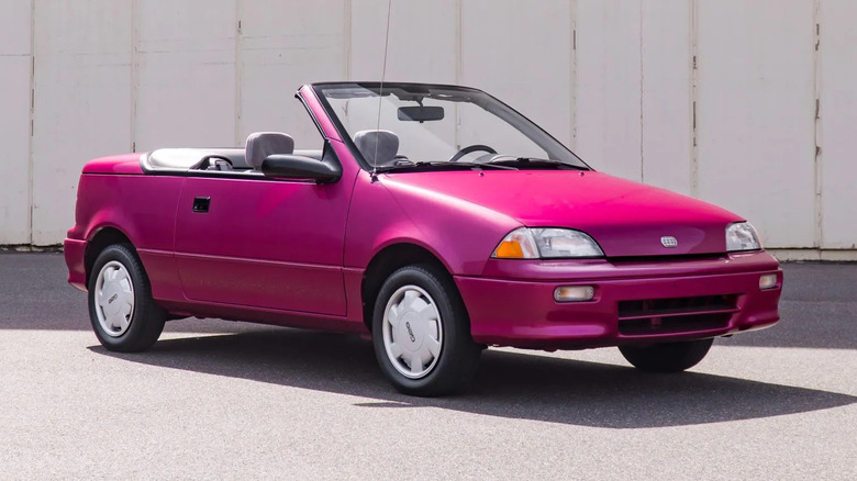 Front three-quarters shot of a Candy Raspberry Geo Metro Convertible with the top down parked in front of a white wall