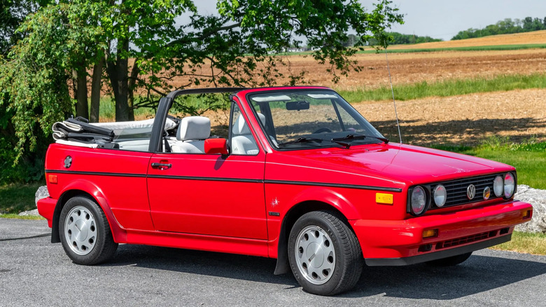 A front three-quarters shot of a pristine red VW Cabriolet parked with the top down in front of a field