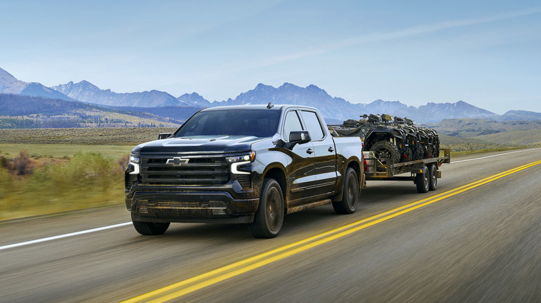 A front 3/4 view of a 2025 Chevrolet Silverado 1500 pulling a trailer with mountains in the background