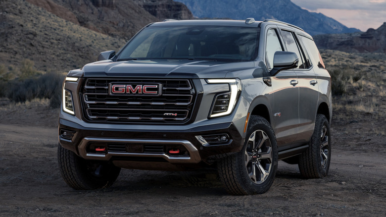 A grey GMC Yukon AT4 Ultimate parked on a dirt road with rock formations behind