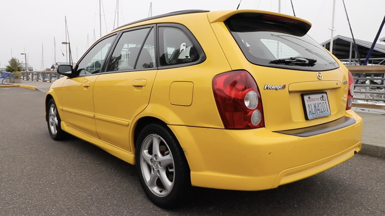A yellow Mazda Protege 5 parked in front of sailboats