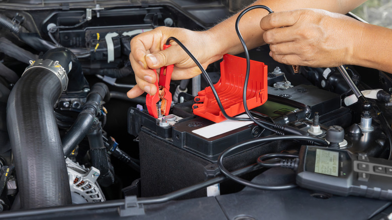 Man is measuring AGM battery power of suv car by battery tester at home.