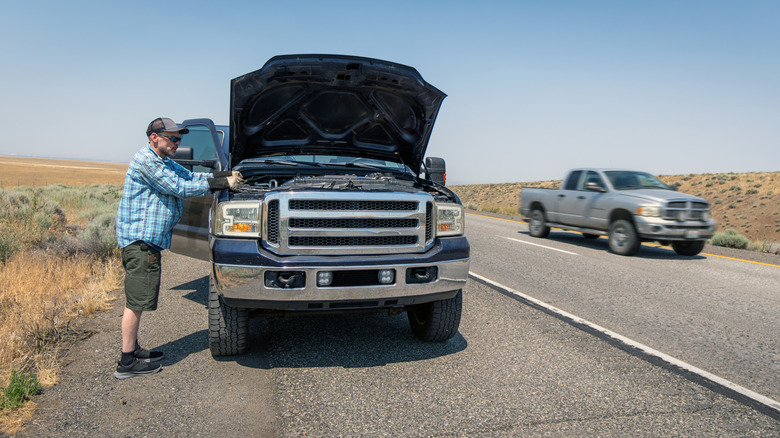 Blue pickup truck breaks down on the shoulder of a freeway while owner tries to assess the problem.