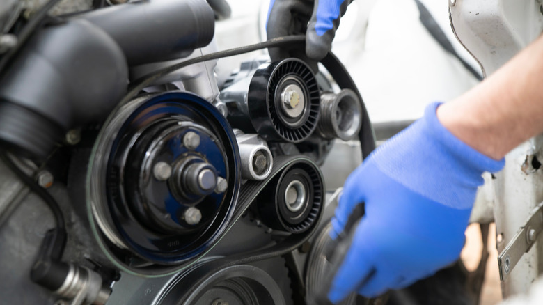 Mechanic Working on Car Timing Belt Replacement Under the Hood in Automotive Workshop