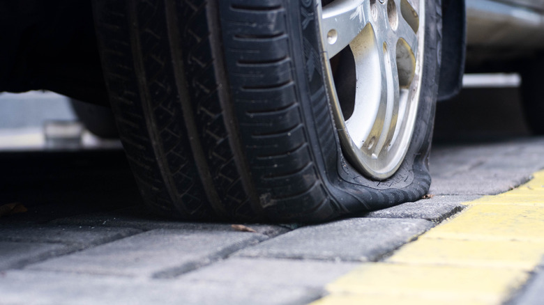 Rear right flat tire of car close-up. tire puncture. Vehicle stands on the road with perforated rubber on a wheel with a metal disc, Air tire pressure lose on the road.