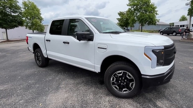 The side view of a 2022 Ford F-150 Lightning Pro parked on a paved surface with trees and buildings in the background