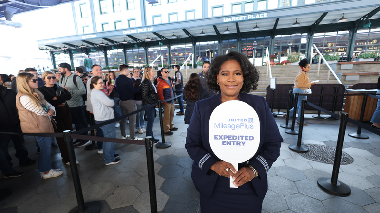 an airline attendant holding a sign for United milage plus