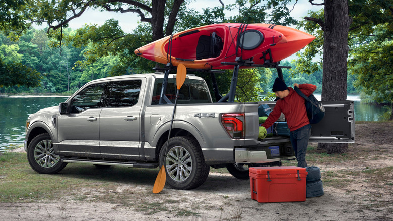 rear three-quarters shot of a silver F-150 parked in front of a lake with red kayaks on a rack over the bed and a man unloading a cooler from the bed