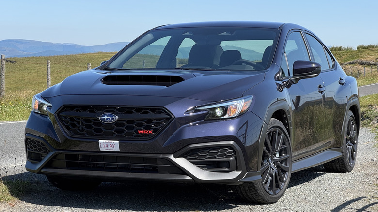 front three-quarters shot of a purple 2026 WRX Base parked on gravel next to a road and in front of grassy hills