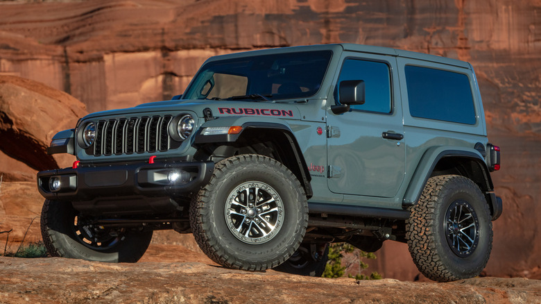front three-quarters shot of a gray Wrangler two-door parked on rock in front of a wall of red rocks