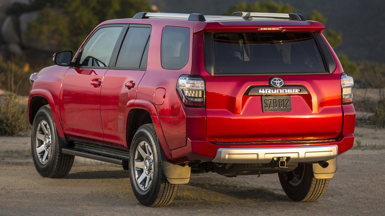 rear three-quarters shot of a red fifth-gen 4runner parked on dirt in front of trees