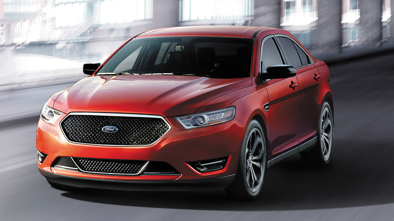 A front three quarters shot of a red Ford Taurus SHO driving under a bridge