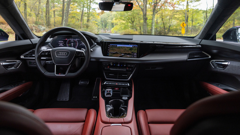 A wide shot of the dashboard and center console in the Audi E-Tron GT with a red interior and trees out the windshield