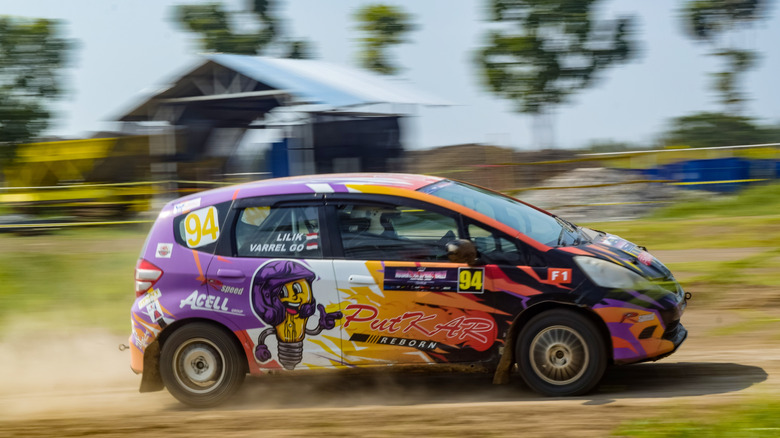 Semarang Indonesia October 19 2025 Honda Jazz or Honda Fit hatchback GE8 rally car speeds through a dusty dirt rally course blurry in motion