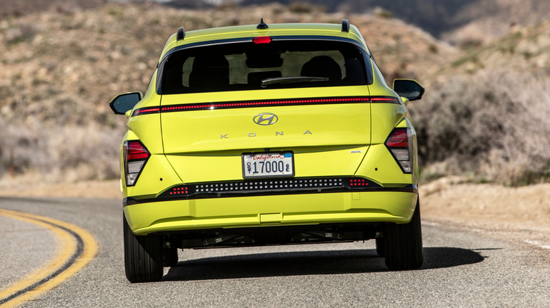 A rear shot of a highlighter yellow Hundai Kona Electric driving on a desert road