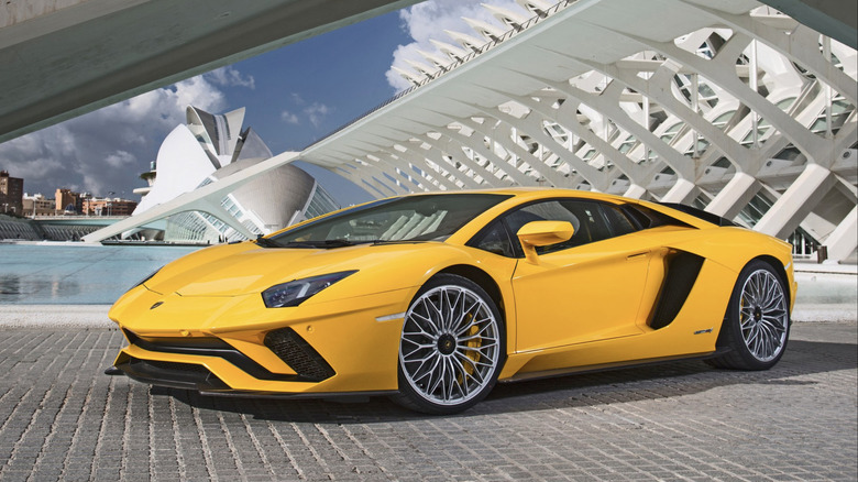 A yellow Lamborghini parked in a cool building with white buttresses on a partly cloudy day