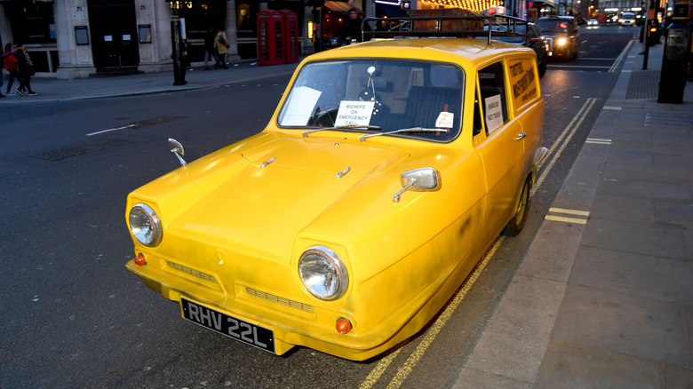 Yellow Reliant Robin parked on a busy city street at a movie premier