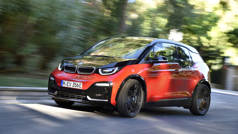 a red and black BMW i3s driving past trees
