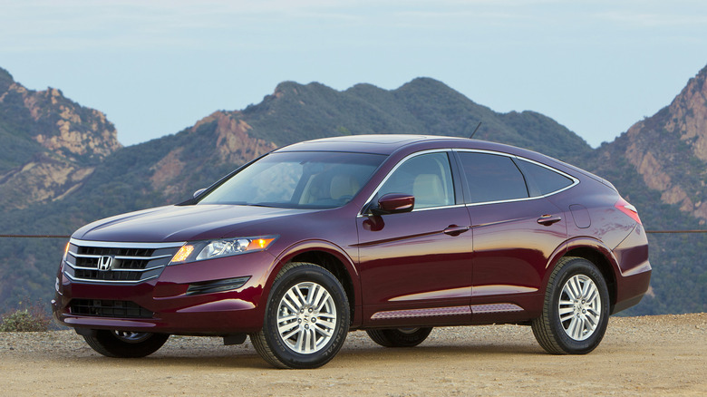 A front three quarters shot of a maroon Accord Crosstour parked on dirt in front of a view of green mountains