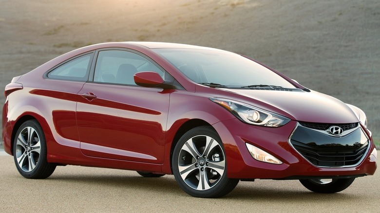 A red Hyundai Elantra coupe parked in front of a dry grassy hill