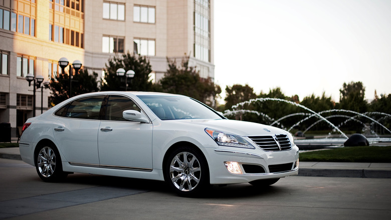 A white Hyundai Equus parked in front of a building with a fountain squirting water